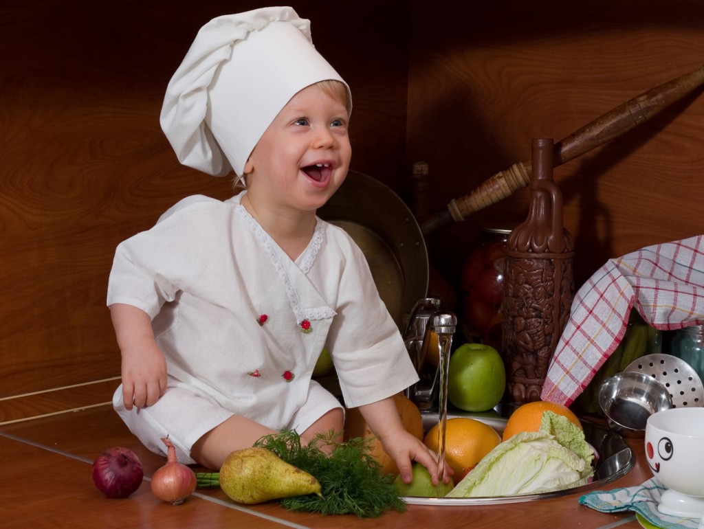 laughing little boy in the cook costume at the kitchen with vegetables